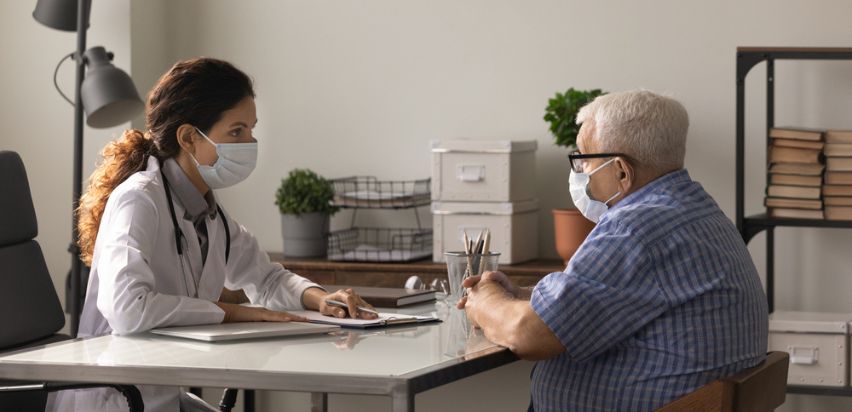 A female doctor and male patient sitting at a desk in a doctor's office.