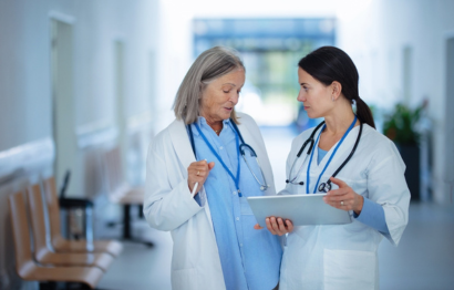 Two female medical professionals in a hospital, discussing a patient chart.