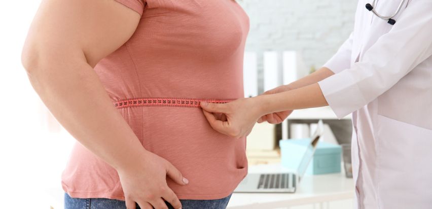 A female medical professional measuring a patient's waist circumference.