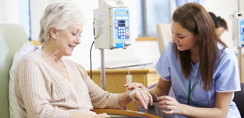 chemotherapy treatment A nurse assists an elderly woman in a hospital setting, providing care and support during her chemotherapy treatment