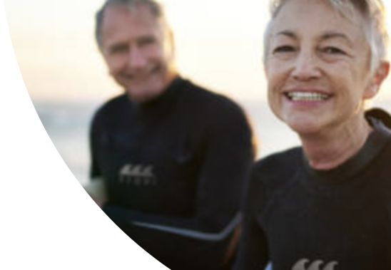 A woman and man wearing wet suits, coming out of the sea.