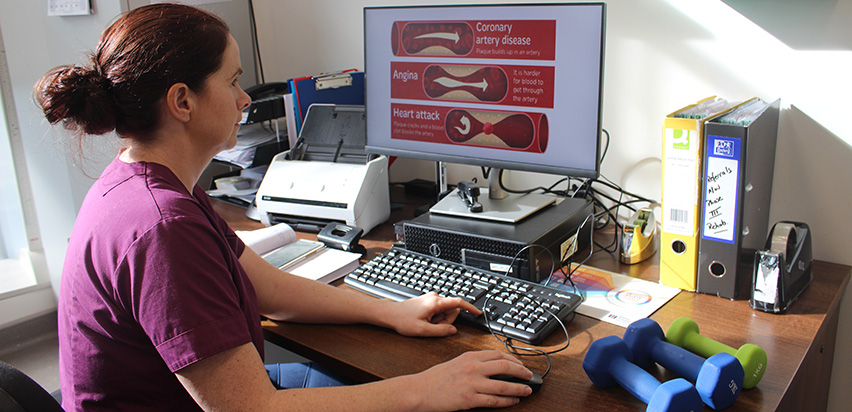 Irne Murphy is looking at a presentation on her computer screen. The presentation is in white and red. It has headings such as coronary artery disease, angina, and heart attack.