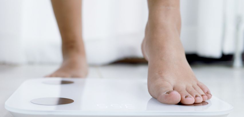 A woman stepping on a weighing scale.