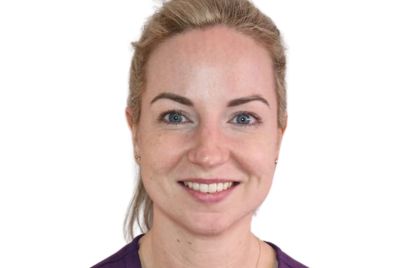 A smiling blonde nurse in a purple uniform.