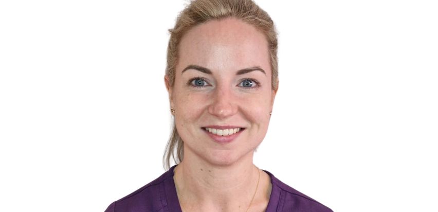 A blonde girl, smiling, wearing purple nursing uniform