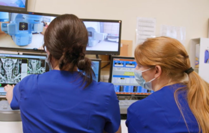Two female radiotherapists overseeing the radiotherapy treatment via computer monitors.
