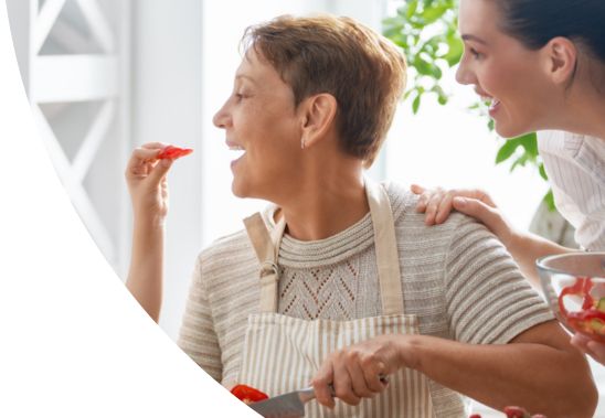 Smiling women chopping vegetables together. A child is feeding her grandmother a piece of food.