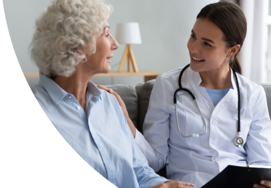 A female doctor and female patient sitting on a couch. The doctor has her hand on the patient's shoulder.