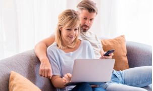 Couple sitting on a sofa, searching for information on their laptop and phone